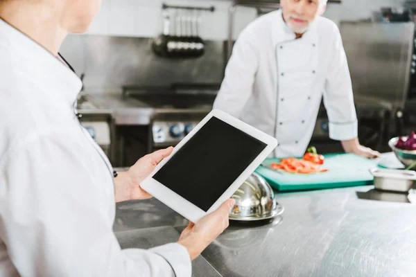 Частичный взгляд на шеф-повара с помощью цифрового планшета с чистым экраном на кухне ресторана — стоковое фото