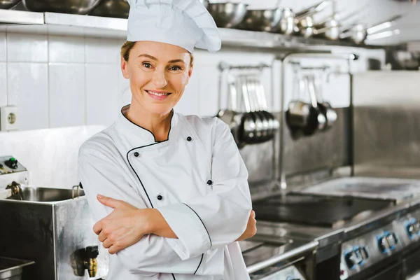 Attractive female chef in uniform with arms crossed looking at camera in restaurant kitchen — Stock Photo