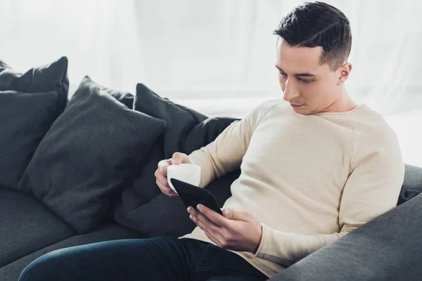 Schöner Mann mit Pokal und Studing mit ebook zu Hause — Stockfoto