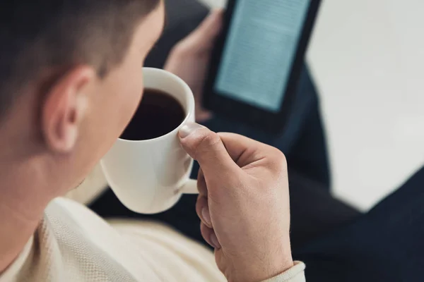 Selective focus of cup with coffee in hand of man studing with ebook — Stock Photo