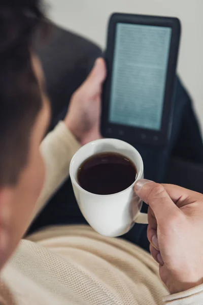 Selective focus of cup with drink in hand of man reading ebook — Stock Photo