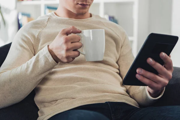 Cropped view of man holding ebook and cup of coffee at home — Stock Photo