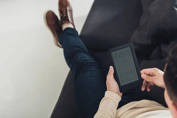 Vista dall'alto dell'ebook di lettura dell'uomo seduto sul divano — Foto stock