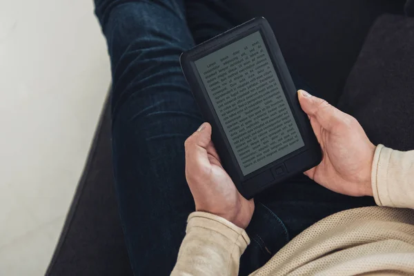 Vue du dessus de ebook dans les mains de l'homme assis sur le canapé — Photo de stock