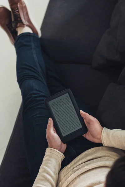 Вид зверху на людину, що навчається з електронною книгою, сидячи на дивані з схрещеними ногами — стокове фото