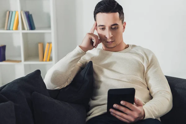 Guapo hombre tachonado con ebook mientras sentado en sofá - foto de stock