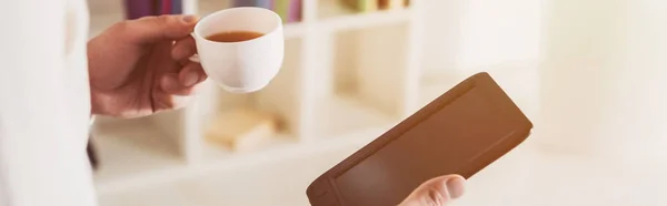 Vista recortada de e-reader y taza de té en manos del hombre - foto de stock