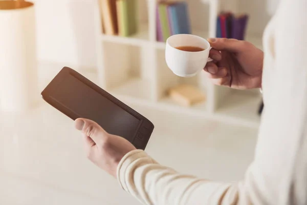 Vista recortada del libro electrónico y la taza de té en manos del hombre - foto de stock