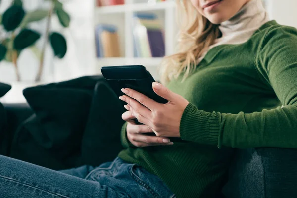 Vue recadrée de femme claquant avec ebook tout en étant assis sur le canapé — Photo de stock