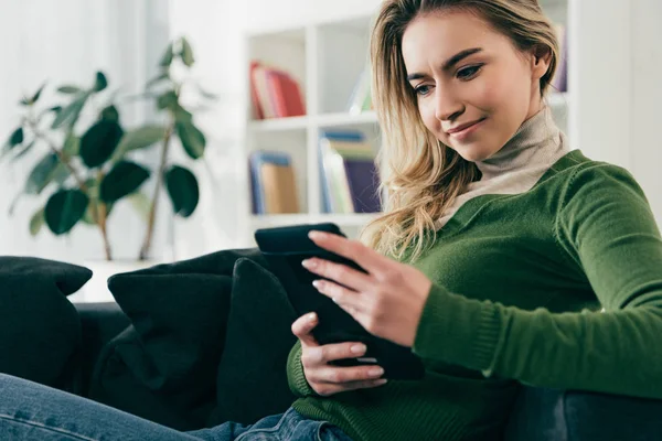 Щаслива жінка навчається з електронною книгою, сидячи на дивані вдома — стокове фото