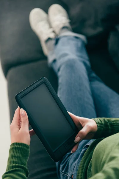 Vista recortada de la mujer sosteniendo ebook con pantalla en blanco mientras está sentado en el sofá - foto de stock