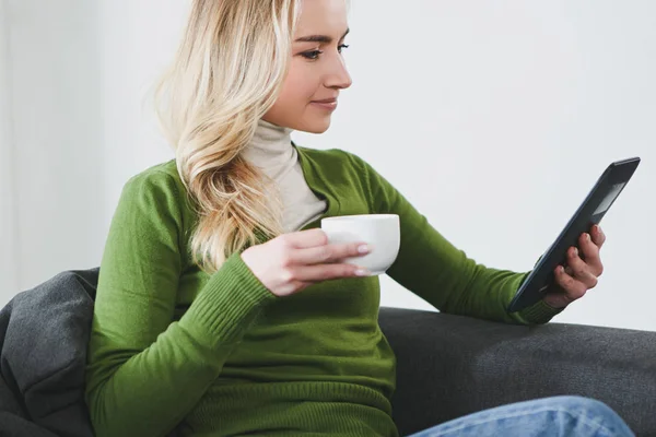 Mulher alegre cravo com e-book e segurando xícara com chá — Fotografia de Stock