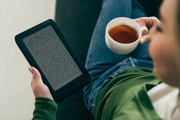 Selective focus of woman holding ebook and cup with tea in hands — Stock Photo