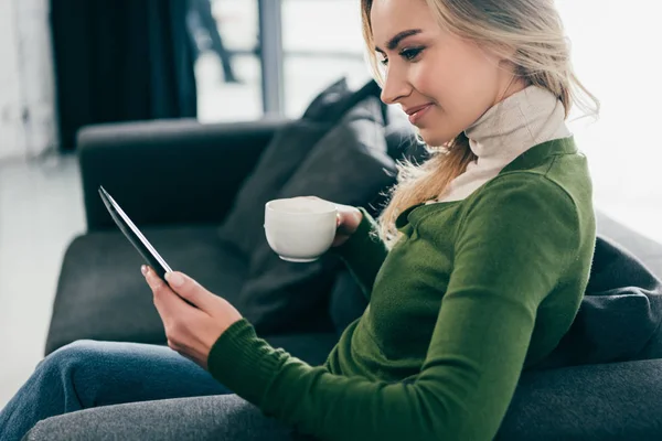 Привлекательная женщина, держащая чашку с чаем во время шипения с электронной книги — стоковое фото