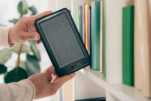 Ausgeschnittene Ansicht eines Mannes, der eBook aus dem Bücherregal nimmt — Stockfoto