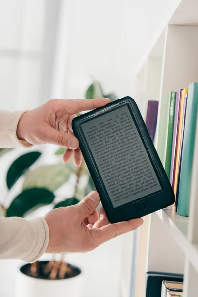 Cropped view of man holding ebook in hands near bookshelf — Stock Photo