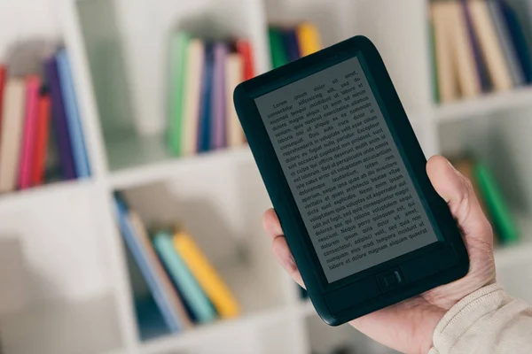 Cropped view of man holding e-reader inear bookshelf — Stock Photo