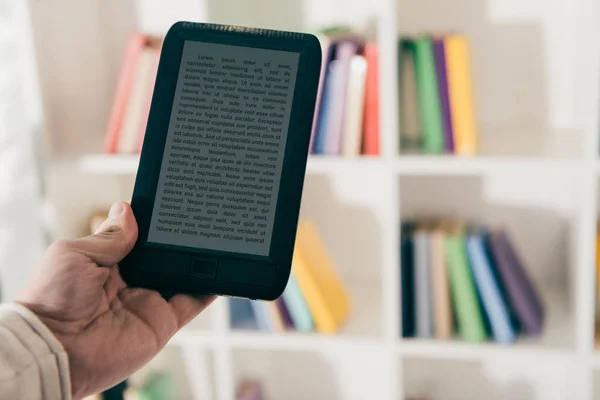 Cropped view of man holding e-book in hand near bokkshelf — Stock Photo