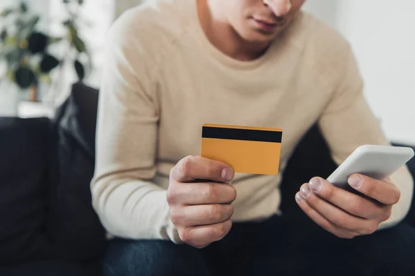 Visão cortada de homem segurando smartphone e cartão de crédito em mãos — Fotografia de Stock
