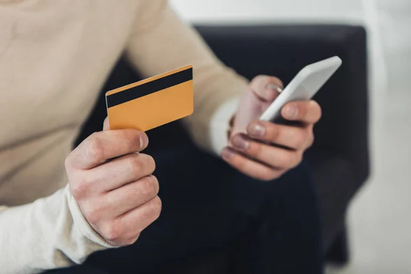 Vista recortada del hombre con tarjeta de crédito y teléfono inteligente en las manos - foto de stock