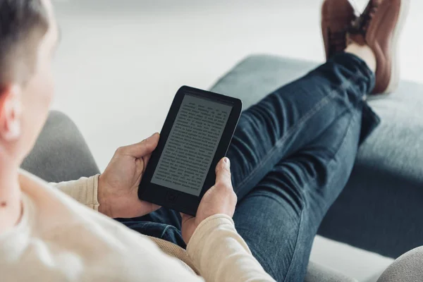 Vue recadrée d'un homme lisant un livre électronique assis dans un fauteuil à la maison — Photo de stock