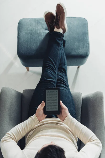 Вид зверху людини, що тримає електронного читача, сидячи в кріслі — стокове фото