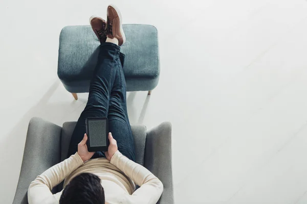 Vista dall'alto dell'uomo che tiene l'e-reader mentre è seduto in poltrona a casa — Foto stock