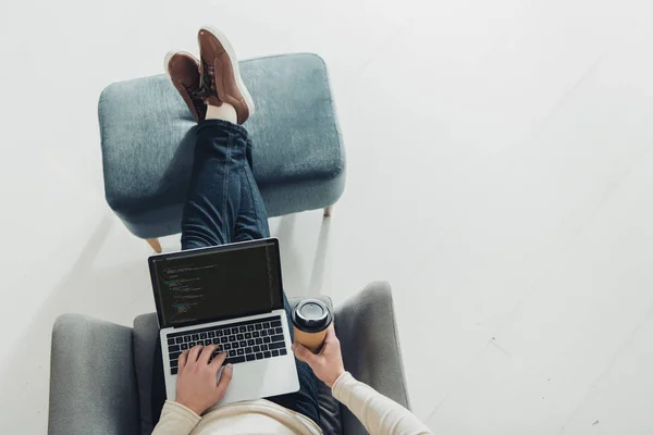 Vista superior del hombre sosteniendo la taza de papel y usando el ordenador portátil con código de computadora en la pantalla - foto de stock