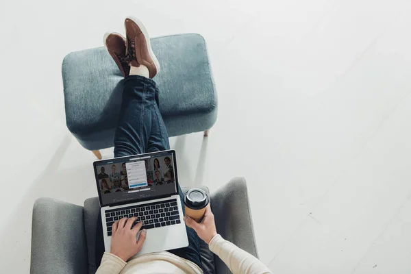 Top view of man holding paper cup and using laptop with linkedin website on screen — Stock Photo