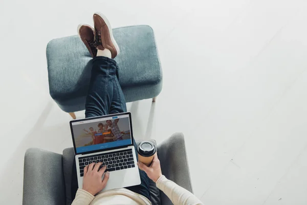 Vista dall'alto dell'uomo che tiene in mano la tazza di carta e utilizza il computer portatile con il sito web di couchsurfing sullo schermo — Foto stock