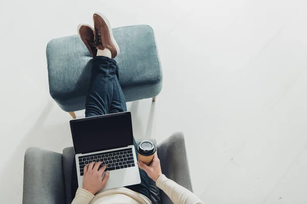 Vue recadrée de l'homme tenant tasse en papier et en utilisant un ordinateur portable avec écran blanc — Photo de stock