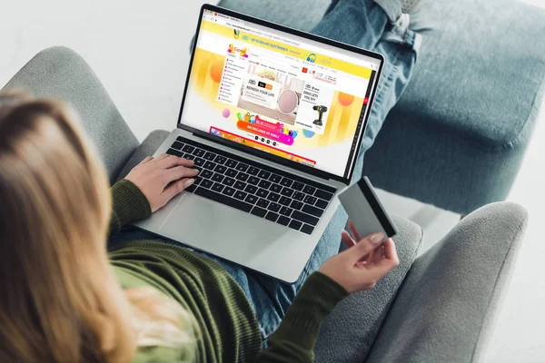 Cropped view of woman holding credit card and using laptop with aliexpress website on screen — Stock Photo