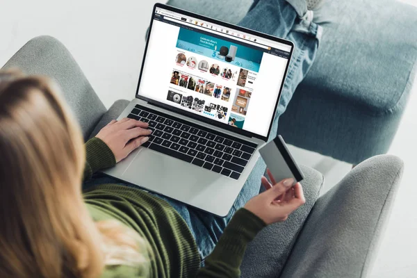 Cropped view of woman holding credit card and using laptop with amazon website on screen — Stock Photo