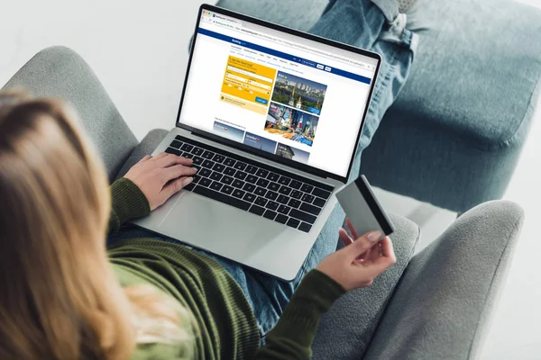 Cropped view of woman holding credit card and using laptop with booking website on screen — Stock Photo