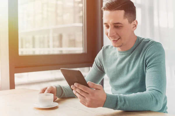 Uomo allegro borchie con ebook e tenendo in mano una tazza di tè a casa — Foto stock