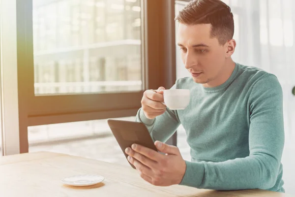 Красивый мужчина, который изучает электронную книгу, держа чашку с чаем — стоковое фото