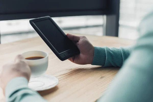 Vista recortada del hombre sosteniendo la taza de té cerca del libro electrónico con pantalla en blanco - foto de stock