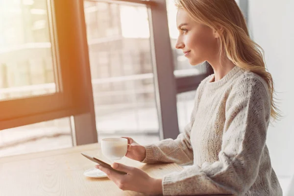 Atractiva mujer mirando a la ventana mientras sostiene la taza con bebida - foto de stock