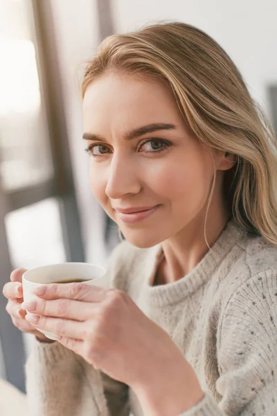 Atractiva mujer sosteniendo taza con té y mirando a la cámara - foto de stock