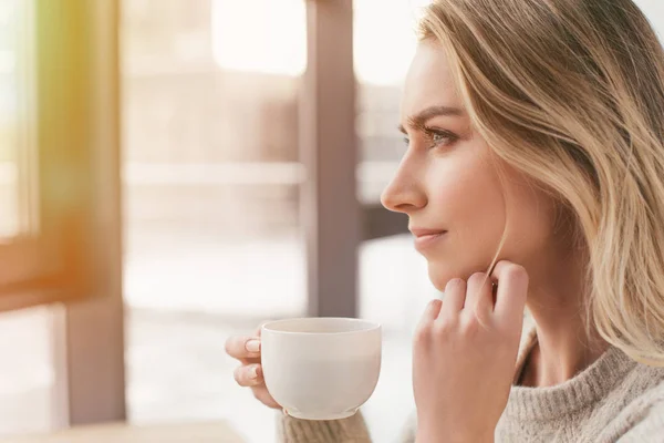 Verträumte Frau blickt auf Fenster und hält Tasse — Stockfoto