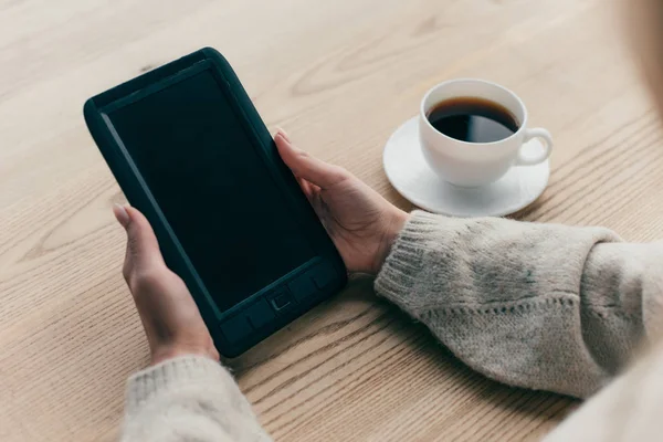 Обрізаний вид жінки, що тримає електронного читача біля чашки кави — стокове фото