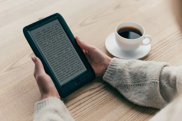 Ausgeschnittene Ansicht einer Frau, die mit E-Book in der Nähe einer Tasse Kaffee sitzt — Stockfoto