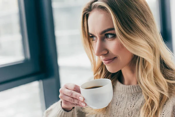 Fröhliche Frau lächelt, während sie Tasse mit Tee in der Hand hält — Stockfoto