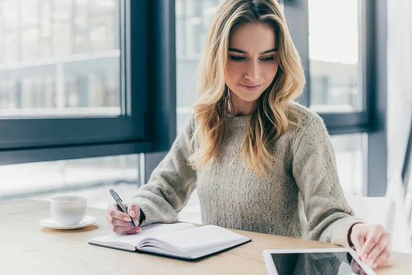 Schöne Frau stopft mit digitalem Tablet und hält Stift in der Nähe von Notizbuch — Stockfoto