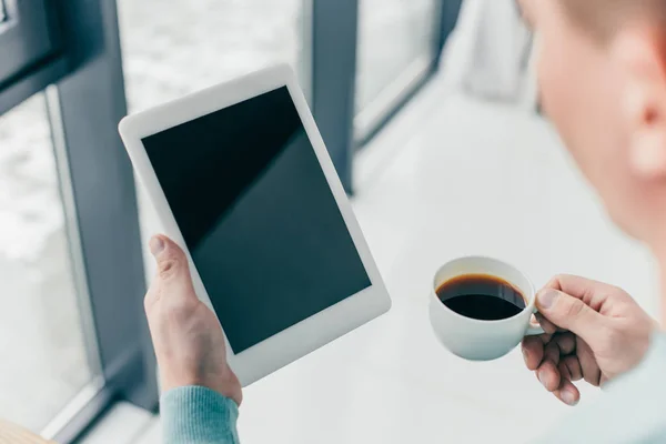 Vista recortada del hombre sosteniendo la taza con café y tableta digital con pantalla en blanco en las manos - foto de stock