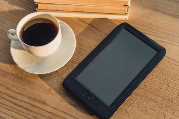 Black e-reader with blank screen lying near cup with coffee on table — Stock Photo