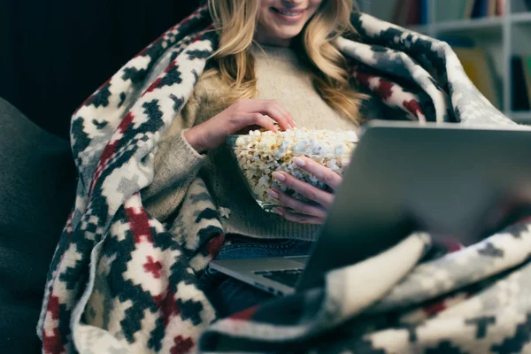 Abgeschnittene Ansicht einer Frau, die sich einen Film auf ihrem Laptop ansieht und eine Schüssel mit Popcorn hält — Stockfoto