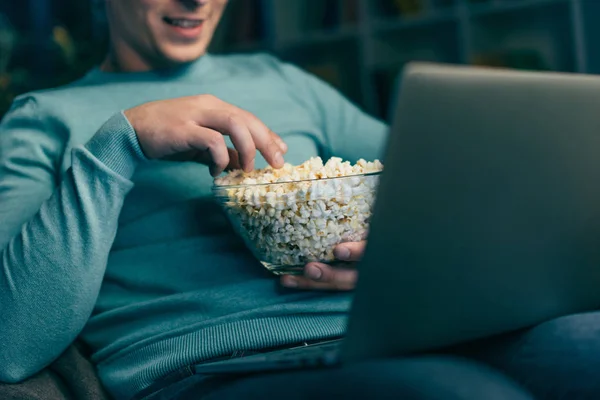 Vue recadrée de l'homme regardant un film sur ordinateur portable et tenant bol avec pop-corn — Photo de stock