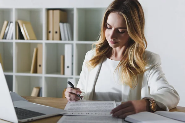 Attrayant femme regardant contrat près ordinateur portable — Photo de stock