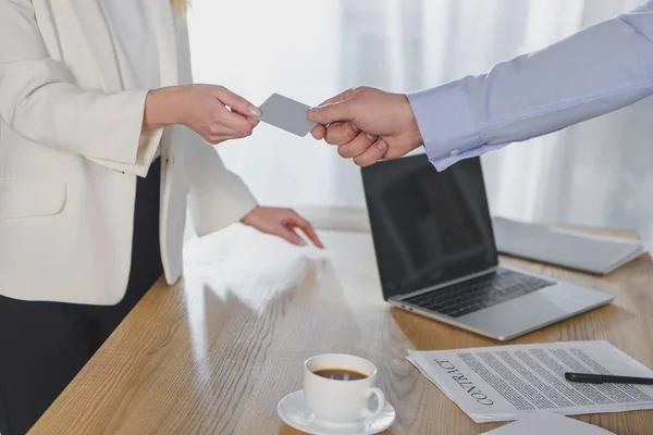 Vista recortada de hombre de negocios dando tarjeta de visita a colega mujer cerca de contrato - foto de stock